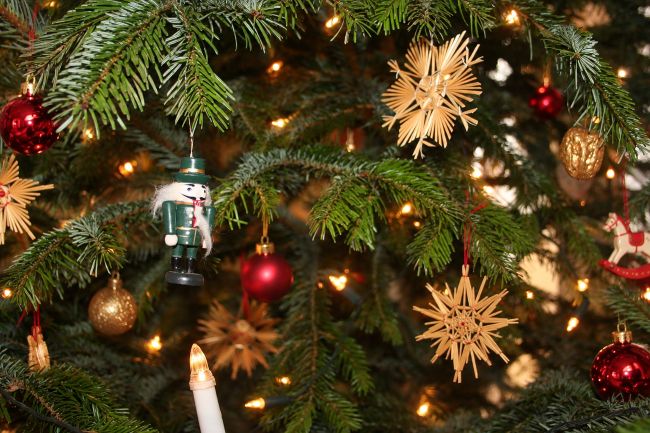 Ein mit Strohsternen, Christbaumkugeln, einer Nussknackerfigur und Lichtern geschmückter Tannenbaum. Das weihnachtliche Bild verbindet Gestaltung und Kultur im Programm des Badischen Landesmuseums.