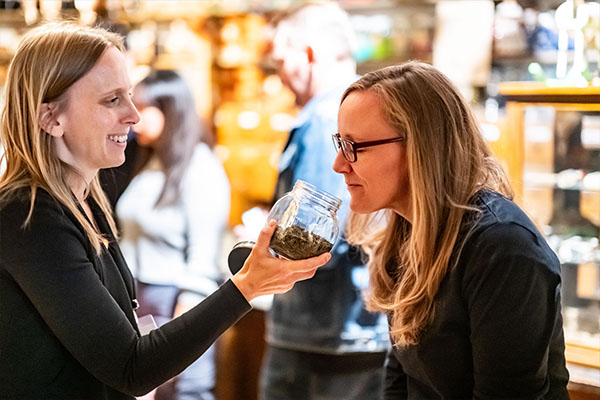 Zwei Frauen stehen im Badisches Landesmuseum im Gespräch, eine hält ein Glas mit Kräutern zum Riechen hoch, sinnliche Vermittlung von Kultur im Museum.
