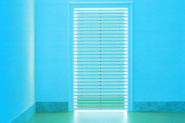 Blau beleuchteter Raum mit einer hellen Lamellentür in der Staatlichen Kunsthalle Baden-Baden. Die atmosphärische Lichtinstallation verweist auf die Veranstaltungsreihe Blaue Stunde und verbindet zeitgenössische Kunst und Kultur mit dem Programm des Badischen Landesmuseums.