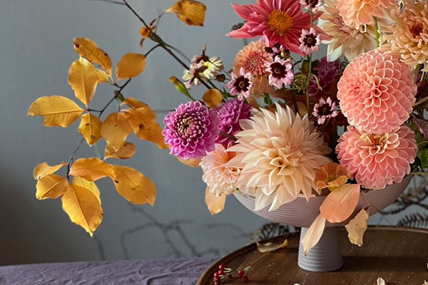 Blumenarrangement mit Dahlien und herbstlichen Zweigen in warmen Rosa-, Creme- und Orangetönen auf einem Tisch. Die florale Inszenierung verbindet Natur, Gestaltung und Kultur im Programm Bloom up! des Badischen Landesmuseums.
