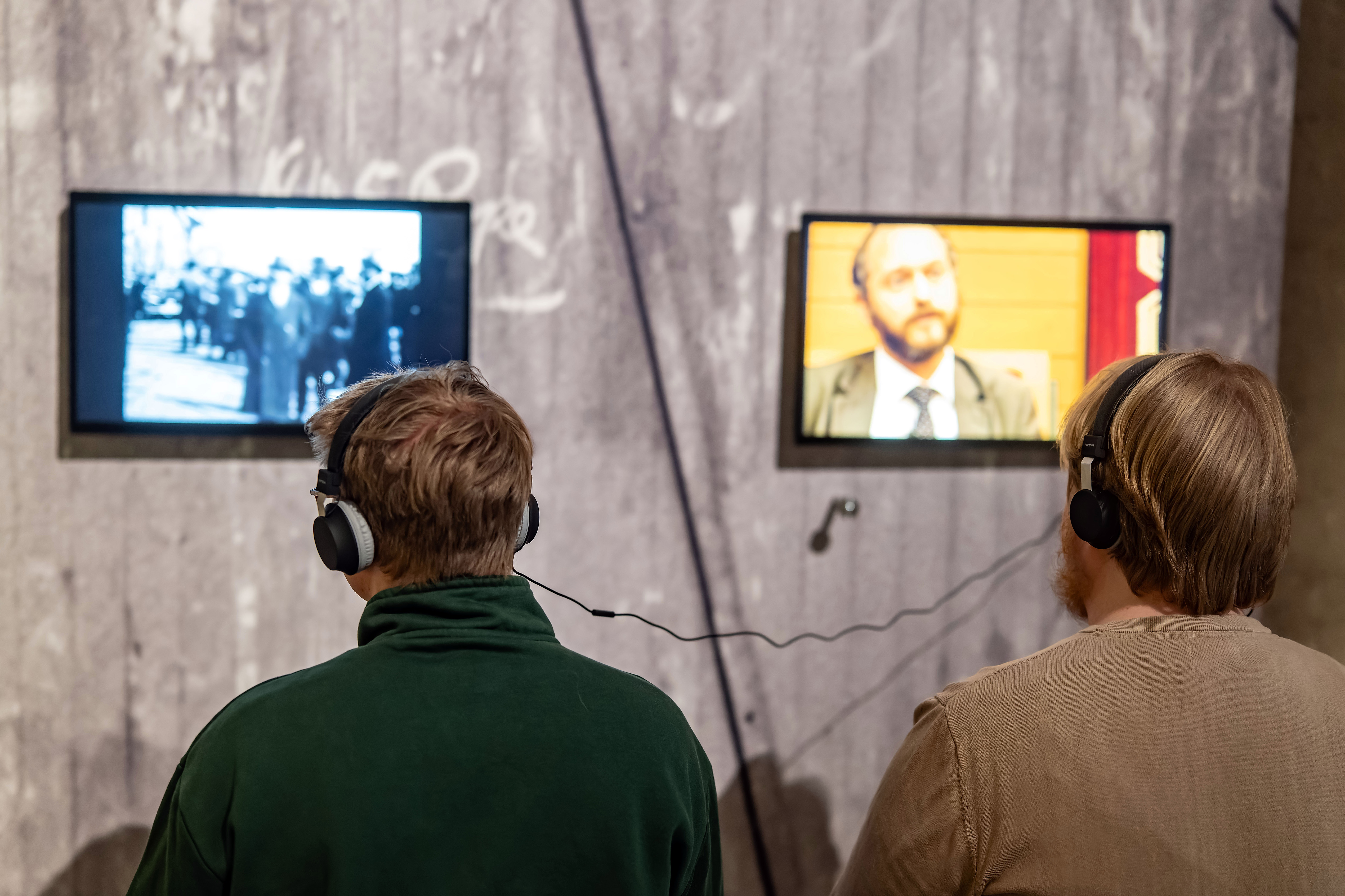 Besucher mit Kopfhörern schauen einen Film in einer Ausstellung