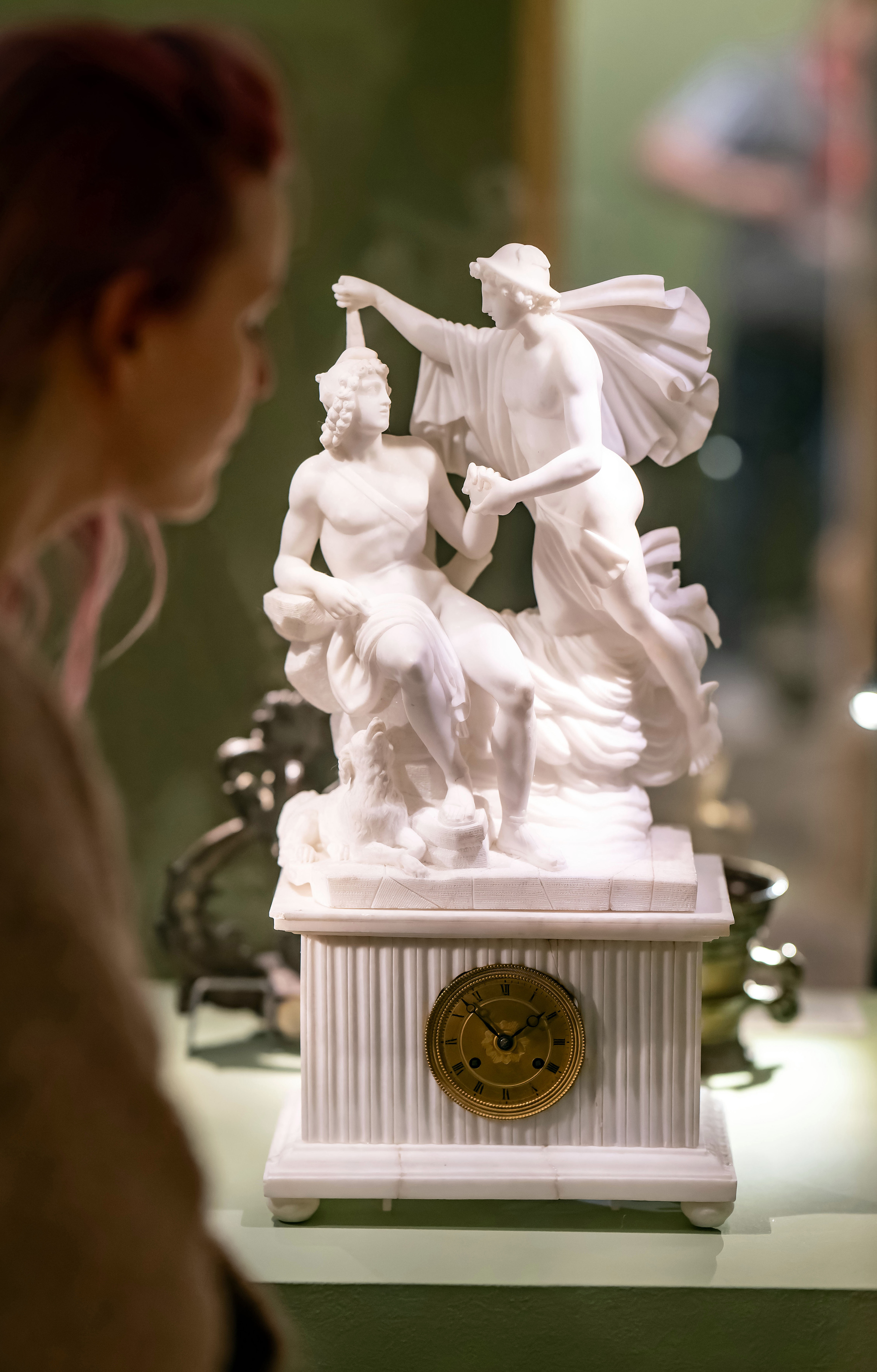 Besucherin betrachtet eine weiße Skulptur, in deren Sockel eine Uhr integriert ist