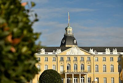 Das Karlsruher Schloss mit seiner gelben Barockfassade und dem markanten Schlossturm im Sonnenlicht. Das historische Gebäude ist Sitz des Badischen Landesmuseums und ein zentraler Ort für Kultur, Ausstellungen und Events in Karlsruhe.