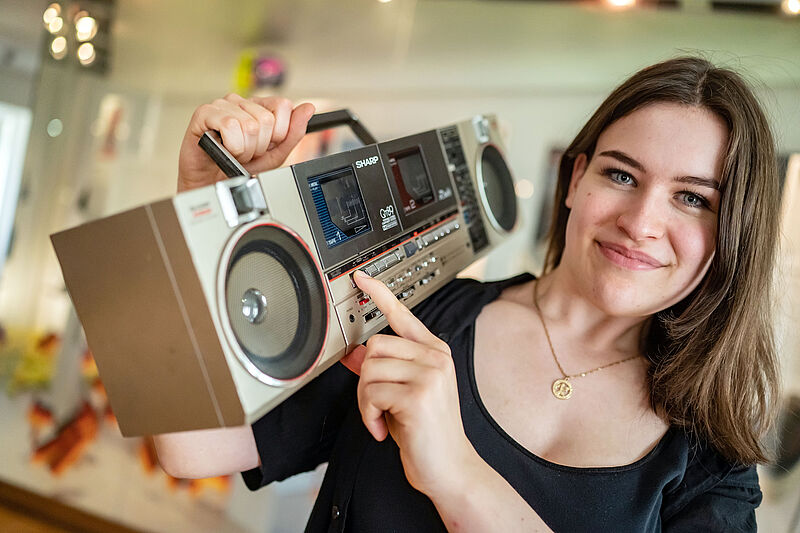 Eine junge Frau posiert mit einem Ghettoblaster auf der Schulter.