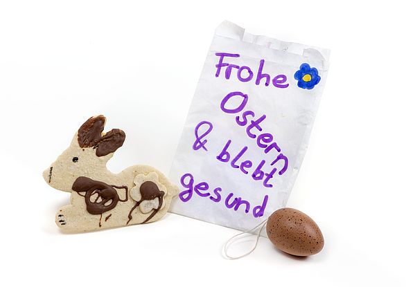 Nachbarschaftsgeschenk zu Ostern 2020 in Coronazeiten: ein selbstgebackener Hase, ein Schoko-Ei und ein handgeschriebener Notizzettel mit dem Text: Frohe Ostern & bleibt gesund