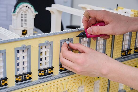 Hände montieren Fensterdetails am Modell des Karlsruher Schlosses aus Klemmbausteinen, Badisches Landesmuseum zeigt Kultur im Entstehungsprozess