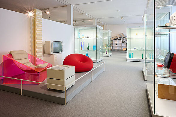 Ausstellungsraum im Badisches Landesmuseum mit Designobjekten, darunter ein transparenter Sessel, ein roter Sitzsack und ein alter Fernseher, Kultur und Alltagsdesign im Fokus.