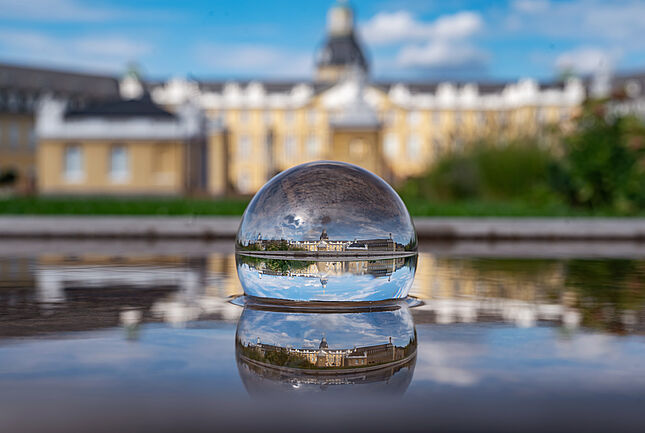 Eine Glaskugel in der sich das Karlsruher Schloss spiegelt und im Hintergrund das Schloss