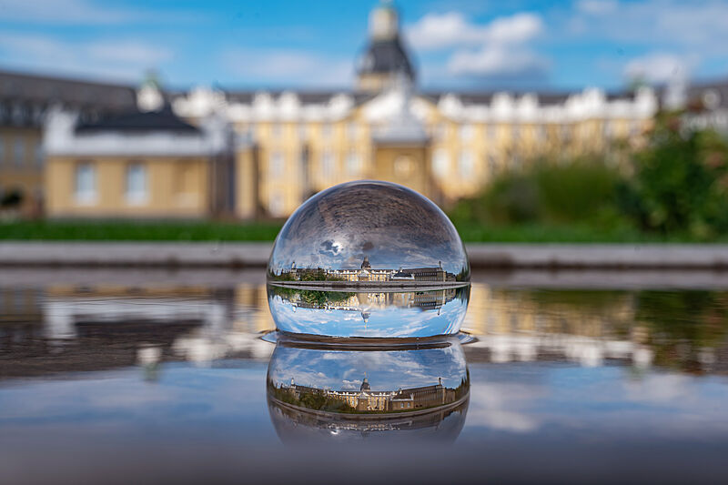 Eine Glaskugel in der sich das Karlsruher Schloss spiegelt und im Hintergrund das Schloss