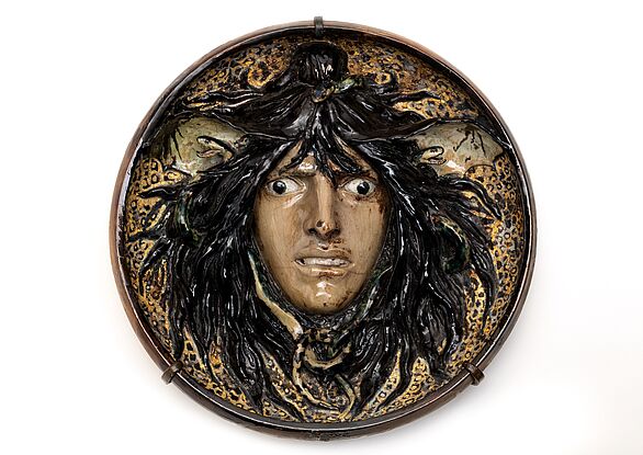 Keramikteller der ein Gesicht mit verdrehten Augen und schwarzem Haar zeigt.