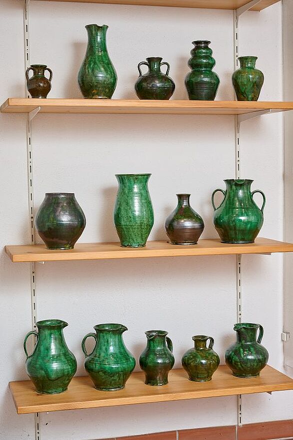 Die Sammlung von Josef Maier im Keramikmuseum Staufen zeigt blau glasierte Keramik mit dekorativen Mustern. Im Mittelpunkt steht ein bauchiger Krug mit weißen und braunen Wellenlinien, flankiert von Tellern und Schalen mit floralen Motiven. Das Badische Landesmuseum präsentiert damit einen Einblick in die keramische Kultur.