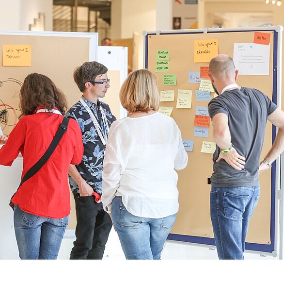 Vier Personen des Bürgerbeirats tauschen sich bei einem Workshop aus und kleben Post-its auf eine Wand.