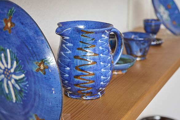 Die Sammlung von Josef Maier im Keramikmuseum Staufen zeigt blau glasierte Keramik mit dekorativen Mustern. Im Mittelpunkt steht ein bauchiger Krug mit weißen und braunen Wellenlinien, flankiert von Tellern und Schalen mit floralen Motiven. Das Badische Landesmuseum präsentiert damit einen Einblick in die keramische Kultur.