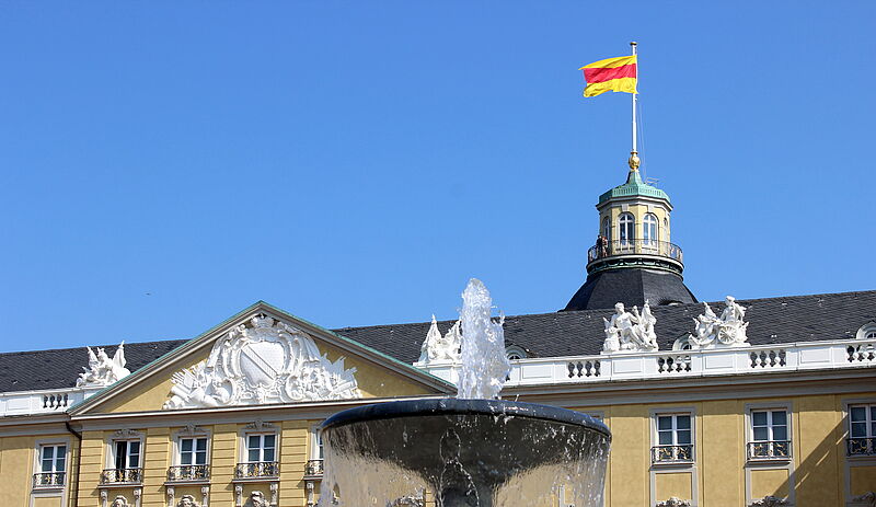 Aussenansicht des Badischen Landesmuseums im Karlsruher Schloss mit badischer Flagge vor blauem Himmel.