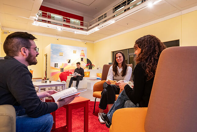 Personen auf einer Sitzgruppe lesen Bücher und unterhalten sich