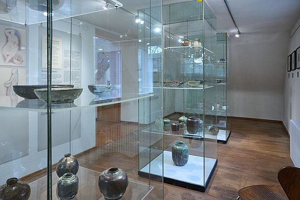 Die Sammlung des Keramikmuseums Staufen präsentiert historische und moderne Keramikkunst in einem hellen Ausstellungsraum mit Holzboden. In raumhohen Glasvitrinen stehen zahlreiche glasierte Vasen, Schalen und Gefäße unterschiedlicher Formen und Farben. Das Badische Landesmuseum vermittelt mit dieser Präsentation Einblicke in die Geschichte des Töpferhandwerks und die vielfältige Keramikkultur.