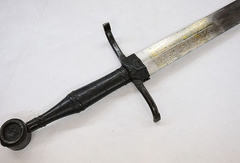 Mittelalterliches Schwert mit gerader Klinge, Parierstange und rundem Knauf, Detailansicht von Griff und Klingenansatz, Sammlung des Badischen Landesmuseums als Zeugnis historischer Waffenkultur.