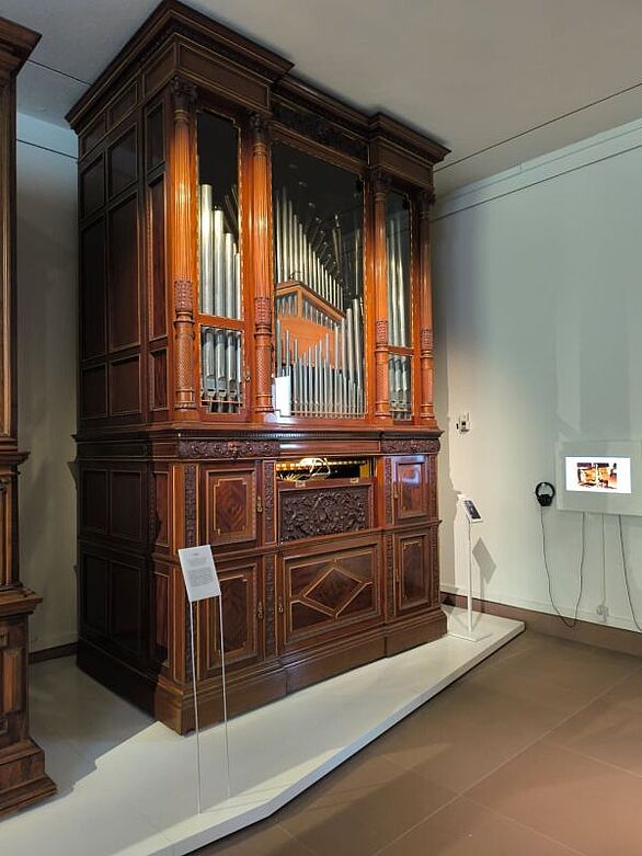 Historische Orgel in einem reich verzierten Holzgehäuse mit sichtbaren Pfeifen im Deutschen Musikautomaten-Museum. Das Badische Landesmuseum präsentiert das Instrument im Rahmen von „Zuhause – Unterwegs“ und vermittelt Kultur, Technikgeschichte und den internationalen Austausch im Orgelbau.
