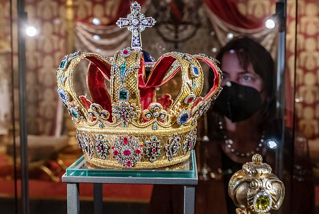 Im Vordergrund die badische Krone, im Hintergrund eine Besucherin mit Maske, die in die Vitrine blickt.