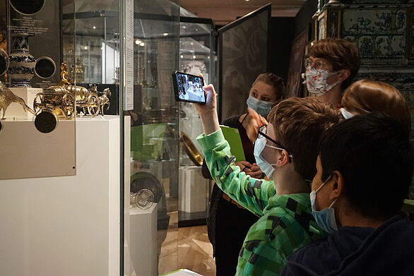 Kinder halten ein Smartphone an die Vitrine und recherchieren zu einem Objekt.