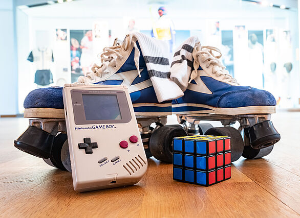 Gameboy, Zauberwürfel und Rollschuhe auf Holzboden