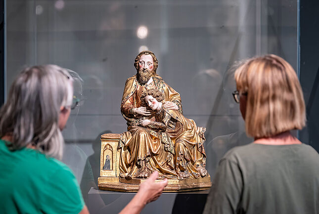 Zwei Besucherinnen betrachten eine Skulptur von Christus und Johannes durch einer Vitrine