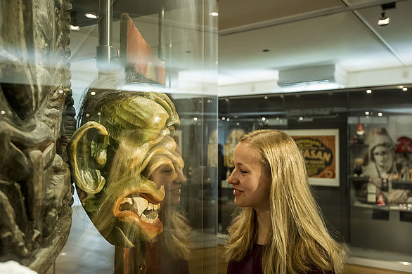 Besucherin betrachtet eine Maske in die Ausstellung "WeltKultur / GlobalCulture"