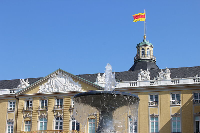 Aussenansicht des Badischen Landesmuseums im Karlsruher Schloss mit badischer Flagge vor blauem Himmel.