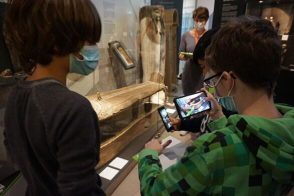 Kinder nutzen ein Smartphone vor einer Vitrine