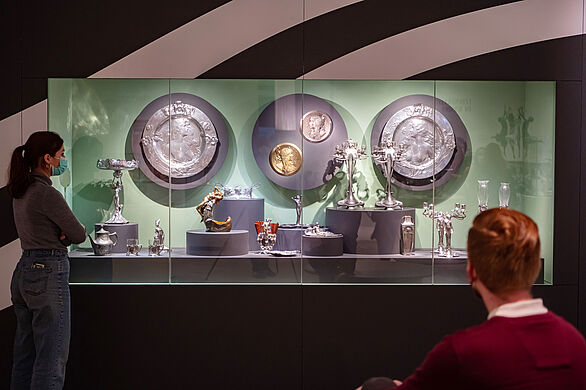 Blick auf eine Vitrine mit Metallgegenständen im Jugendstil. 