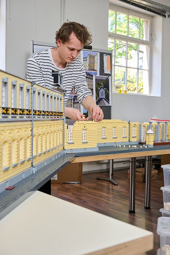 Person baut am großformatigen Modell des Karlsruher Schlosses aus Klemmbausteinen im Atelier, Badisches Landesmuseum zeigt Kultur und Bauprozess