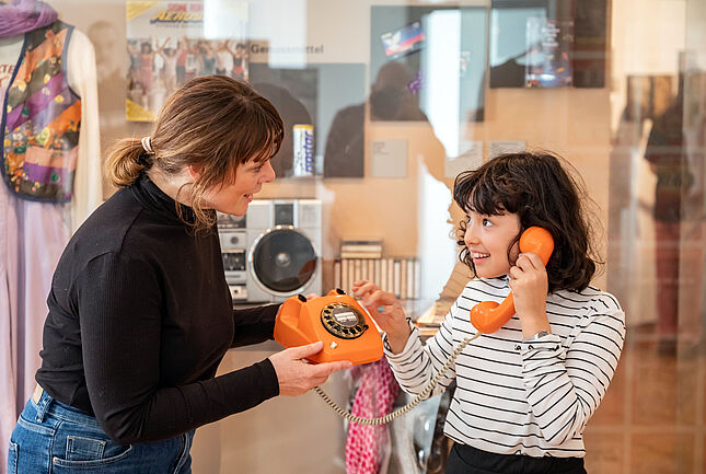 Frau zeigt Mädchen orangefarbenes Telefon mit Wählscheibe