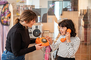Frau zeigt Mädchen orangefarbenes Telefon mit Wählscheibe