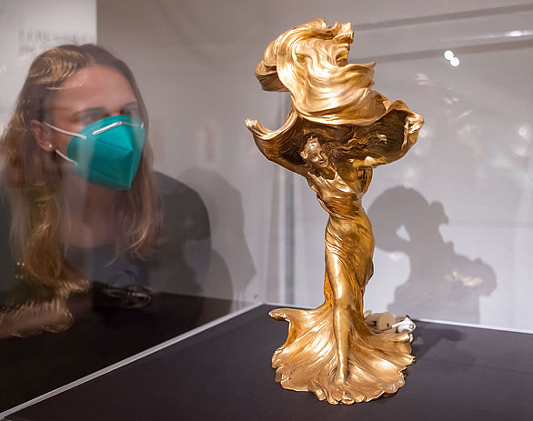 Eine Besucherin blickt in eine Vitrine, in der die goldene Fuller-Lampe ausgestellt ist