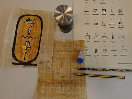 Auf einem Tisch liegen Papyrus, Bleistift, Schreibgriffel und Abbildungen von Hieroglyphen im Alten Ägypten.