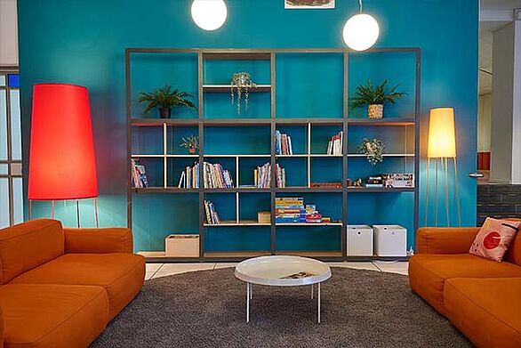 Loungebereich im Badisches Landesmuseum mit Sofa, Regalwand und Büchern vor türkisfarbener Wand, ein Ort zum Verweilen und zur Auseinandersetzung mit Kultur.