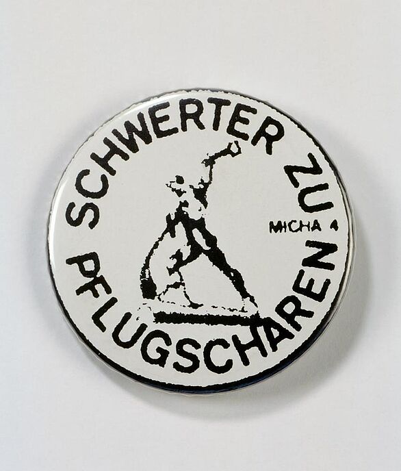 Button mit dem Schriftzug "Schwerter zu Pflugscharen" um das dazugehörige Symbol