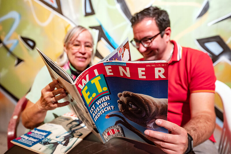 Zwei Personen blättern in einer Zeitschrift der 1980er.