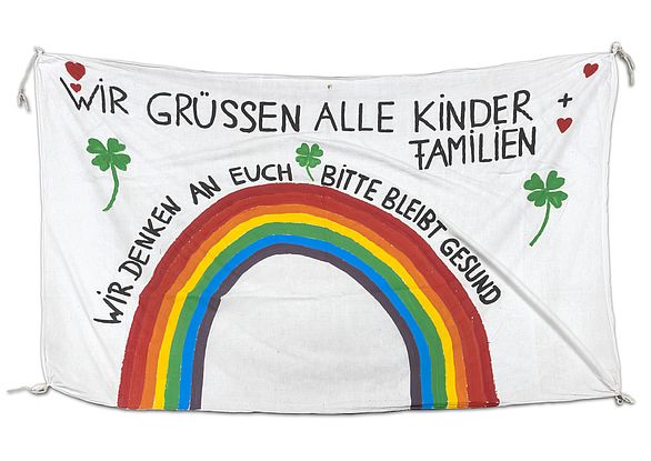 Ein großes Grußbanner der Erzieherinnen des Karlsruher kath. Kindergartens St. Matthias an seine Kinder und ihre Familien mit einem Regenbogen und dem Text: "Wir grüssen alle Kinder + Familien/ Wir denken an euch / Bitte bleibt gesund".